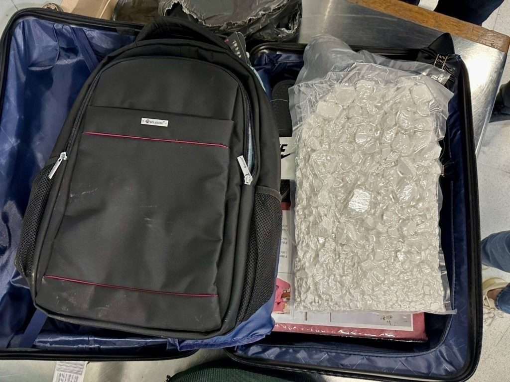 Packages of white powder hidden inside a backpack and bedding set within a black hard shell suitcase.